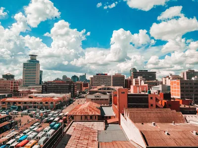 Harare's city-centre skyline of office towers rises above red-roofed buildings under a sky of billowing white clouds.