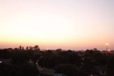 A pink and orange twilight sky glows over the rooftops and treetops of Highfield, Harare.