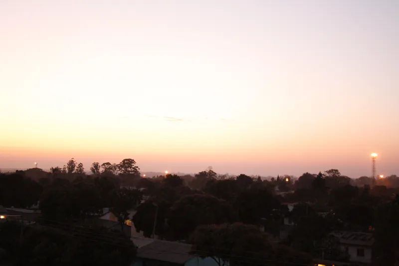 A pink and orange twilight sky glows over the rooftops and treetops of Highfield, Harare.