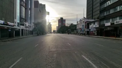 Low evening sun flares between the buildings at the end of an empty Jason Moyo Avenue in Harare's city centre.